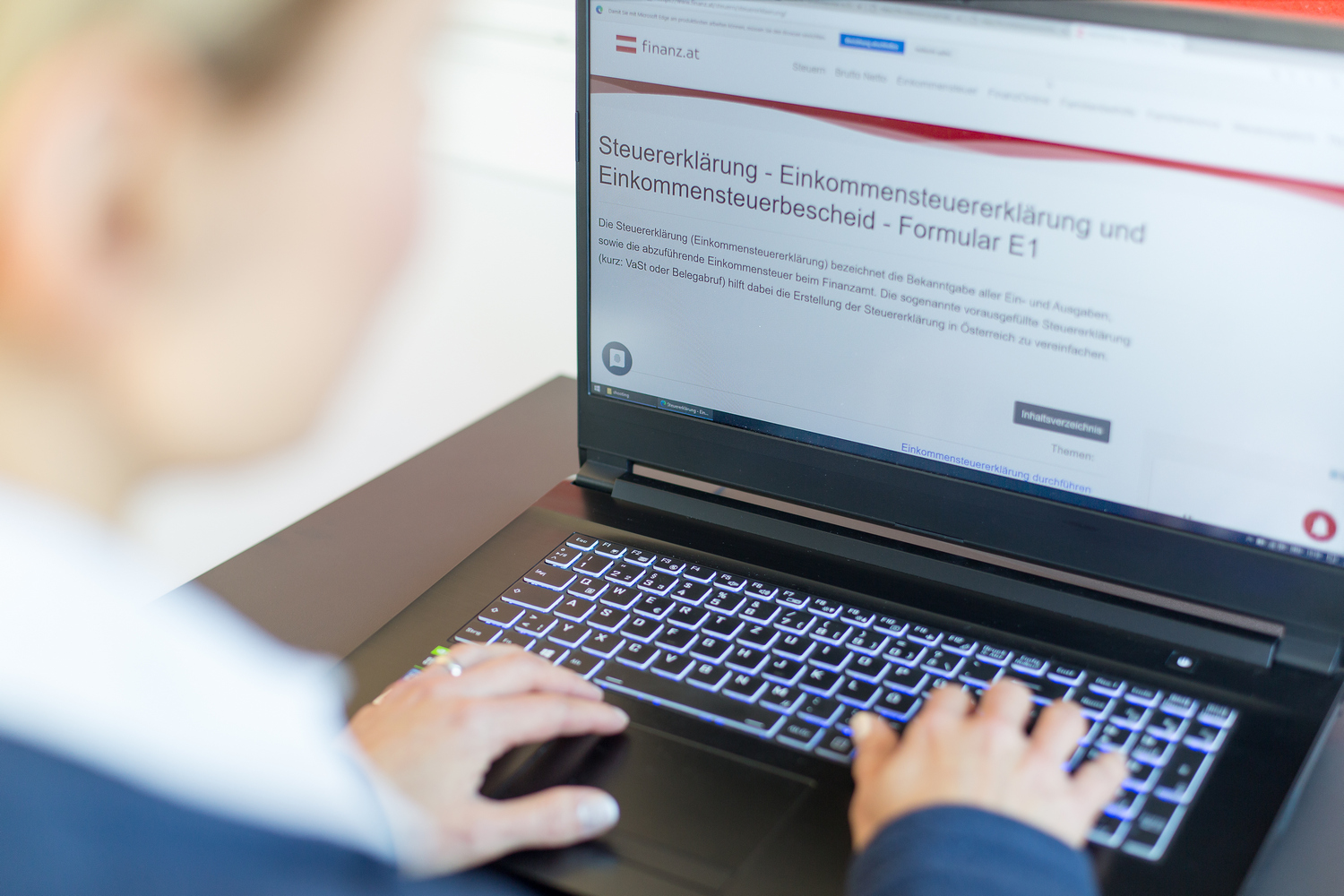 Eine Frau sitzt für einem Laptop und schaut sich im Internet eine Website über Steuererklärung an.